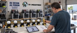 Dominique Droniou pose un trophée doré au bout d'une rangée de trophées à lauriers, dans l'atelier TH Industries : la création de trophée personnalisé, du dessin au podium